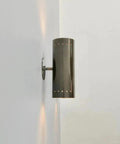 Perforated Brass Wall Sconce - Modern Cylinder Lamp mounted on wall, showcasing sleek cylinder design and decorative light patterns.