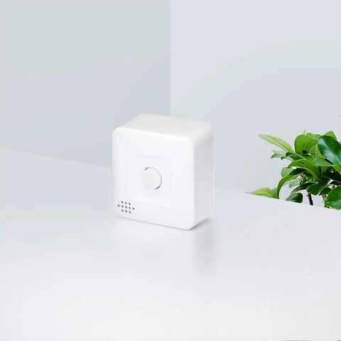 White smart motion sensor for home automation and security with Zigbee, triggers lighting scenes, shown on a table