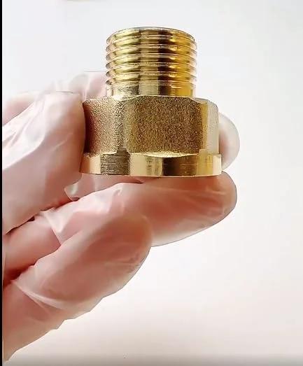 Brass pipe reducer adapter close-up held by gloved hand, threaded male connector and hex body