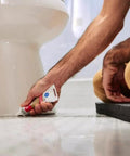 Person applying Advanced Silicone Caulk For Kitchen And Bathroom White 2.8 Fl Oz Tube 1 Pack to floor edge near a toilet on tiled surface.