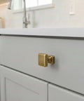Brushed Antique Brass One Inch Square Cabinet Knob set on modern white kitchen cabinet, sleek contemporary look.