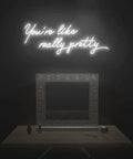 You're like really pretty neon sign above vanity table with mirror in dark room, LED neon tubing glowing softly.
