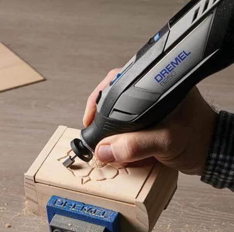 Dremel 8250-5 cordless rotary tool with blue logo, carving wood in a vise (close-up).