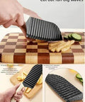 Front view of a black luvilly1 11.4-inch crinkle cutter knife for vegetables on a wooden cutting board.