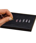 Close-up of Waytest 18K gold testing kit; hand holds small gold sample over black foam tray with color swatches.