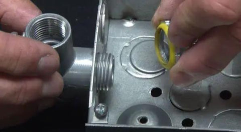 Hands installing Heavy Duty Two Inch Sealing Lock Nut For Electrical Conduit with yellow PVC gasket into metal electrical box.