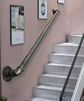 Heavy Duty Badass Wrought Iron Pipe Stair Handrail For Indoor Outdoor Use Rock Solid Wall Mount Banister For Decks Porches And Basements With Durable Bronze Finish mounted on a wall beside gray marble stairs.