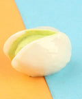 Close-up of a single resin pistachio from the 15-Piece Realistic Miniature Nut Set For Dollhouses on a colorful background.