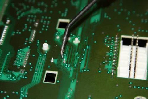 Close-up view of a green automotive circuit board with solder pads and a white connector