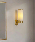 Single Natural Alabaster Rock Wall Sconce With Polished Brass Trim Features E14 Socket And Game Changer Soft Glow To Bring Killer Vibes To Bathrooms Bedrooms Halls As Sleek Wall Fixture on a light wall next to a mirror.