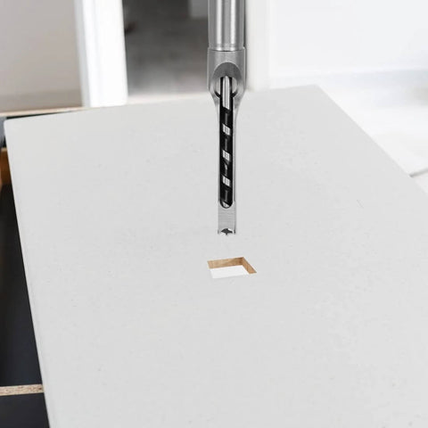 Front view of uxcell 1/2 in hollow mortise drill bit, high-carbon steel, above a square mortise on a white worktable.