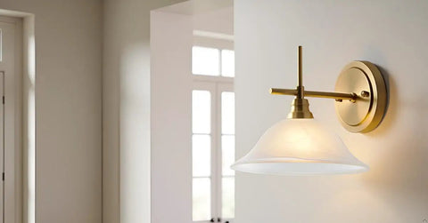 Wall-mounted light fixture with a brass arm and frosted glass shade in a minimalist room.