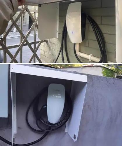 Rugged Outdoor Wall Mount EV Charger Enclosure Shields Tesla Cables During Heavy Rain Hella Waterproof Housing Blocks Wind And Freezing Temperatures Keeps Plugs Safe Now with visible plug and cord in a protective metal case.