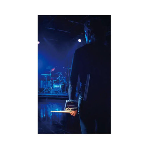 Musician holding Compact Acoustic Drum Trigger Module With 162 Ready To Play Pro Sounds, facing a stage setup.