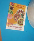 Four Stackable Tray Food Dehydrator And Jerky Maker For Homemade Healthy Snacks Smooth Operation Top Grade Kitchen Essential Recipes book on blue background.