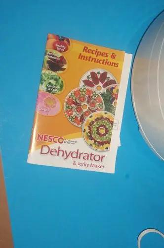 Four Stackable Tray Food Dehydrator And Jerky Maker For Homemade Healthy Snacks Smooth Operation Top Grade Kitchen Essential Recipes book on blue background.