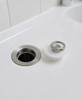 White Round Drain Stopper for Bathtubs and Kitchen Sinks next to a stainless steel drain in a modern sink.