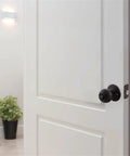 White door with Keyed Entry Ball Door Knob in Matte Black Finish with Brass Construction 2 Way Latch Anti Bump Technology visible
