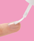 Applying Brush On Nail Glue For Press On Nails 5G, Fast Drying, Strong Hold Bond For Repairs on a natural nail against pink background.