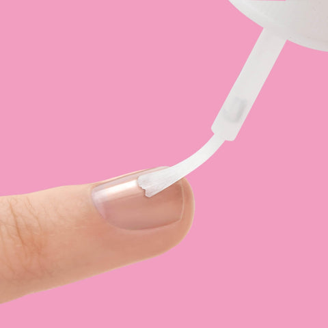 Applying Brush On Nail Glue For Press On Nails 5G, Fast Drying, Strong Hold Bond For Repairs on a natural nail against pink background.