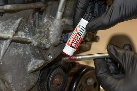 Close-up of gloved hands applying Loctite 37701 red high-strength threadlocker stick (9 g) to an engine bolt