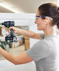 Woman using Built Tough 18V Compact Cordless Drill Workhorse Kit to assemble furniture in a workshop.