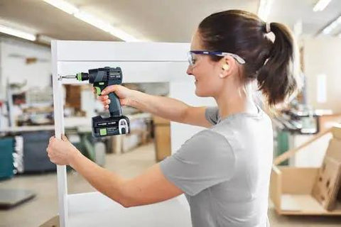Woman using Built Tough 18V Compact Cordless Drill Workhorse Kit to assemble furniture in a workshop.