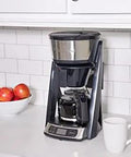 Heat N Brew 10 Cup Programmable Coffee Maker With Stainless Steel Finish on kitchen counter next to a cup and apples