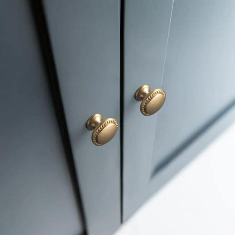 Close-up of two champagne bronze cabinet knobs with wheatear border on navy door, part of set Of 12 Modern Champagne Bronze Cabinet Knobs With Wheatear Border, Classic Round Design For Kitchen Drawers And Dresser Handles, Dope Contemporary Hardware That Elevates Your Home Reno