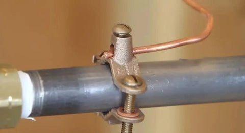 Heavy Duty Bronze Water Pipe Ground Clamp Fits One Quarter To Two Inches attached to metal pipe with copper wire.
