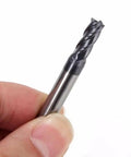 Close-up of AlTiN-coated solid carbide end mill, 4-flute, held between fingers for scale.