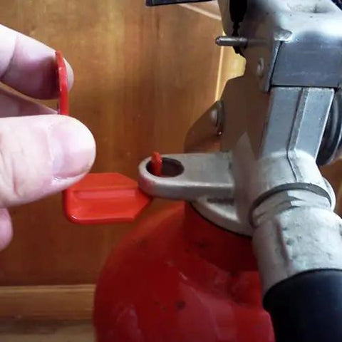 Hand removing safety tag from 5 lb fire extinguisher, showing red design for 100 Pack 5 Lb Fire Extinguisher Wall Brackets Universal Red Mount Holder Indoor Outdoor Heavy Duty Rack Bracket Solid Construction Made In Usa The Real Deal For Home Safety.