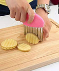 Close-up of pink-handled stainless-steel crinkle cutter slicing ridged veggie rounds on a wooden cutting board