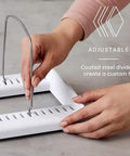 Hands adjusting steel divider on StoreMore Adjustable Bakeware Rack With Steel Wires Seven Adjustable Dividers in kitchen setting.