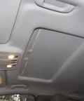 Installed automotive headliner fabric panel; gray car interior with overhead console lights.