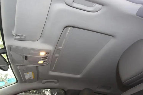 Installed automotive headliner fabric panel; gray car interior with overhead console lights.