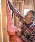 Top Ticket R-13 Pink Kraft Faced Fiberglass Insulation Roll Crafted For Smooth Sailing 2by4 Wall Install To Lock In Warmth Dead Silence And Keep Your Place Snug Year Round Formaldehyde Free Ultra Comfortable Triple Pack being installed by a man.