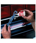 Hands holding Killer Strength Quick Fix Super Adhesive For Plastic Metal Glass Auto Marine Applications with metal tool on a car.