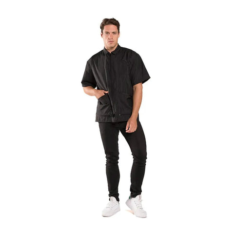 Sleek Black Barber Jacket With Zippered Front And Contrast Pockets Xl Nylon Short Sleeve Top For Salons worn by a man standing with one hand in pocket.