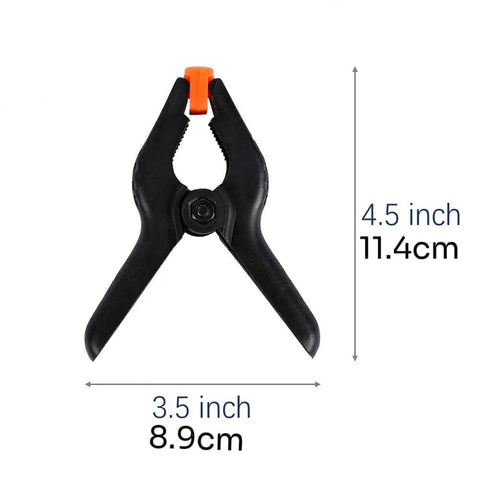 Front view of a black 4.5-inch plastic spring clamp with an orange jaw tip for photography and backdrop setups