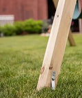 Close-up of a heavy-duty swing set ground anchor securing a wooden playset leg to the grass, part of Playset Anchor Kit For Swing Sets Heavy Duty Ground Anchors That Keep Your Set Rock Solid Stationary And Safer For Outdoor Fun Easy Install Swing Set Hardware To Secure Play Equipment And Protect Your Kids.