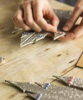 Cricut Knife Blade and Drive Housing; hands arrange silver metallic craft shapes on wooden table beside blade tool