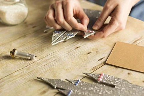 Cricut Knife Blade and Drive Housing; hands arrange silver metallic craft shapes on wooden table beside blade tool