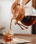 Pouring iced coffee from a portable cold brew coffee maker with slow drip tower into a glass.