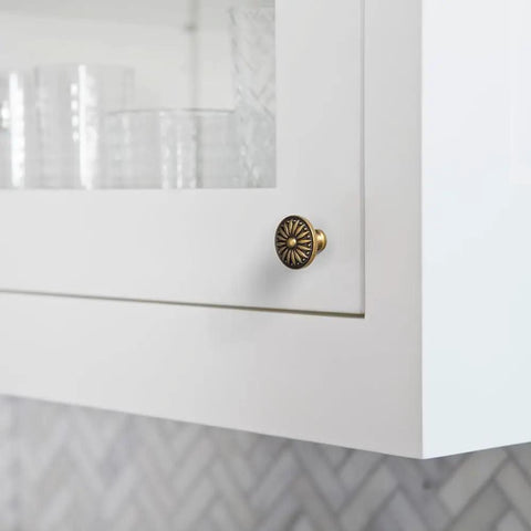 Close-up of Vintage Antique Brass Sunburst Cabinet Knob on white kitchen cabinet, showing distressed floral design.