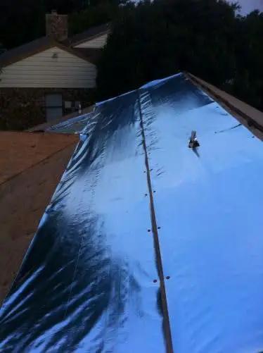 Four By Two Hundred Fifty Foot Synthetic Roof Underlayment Pro Grade Heavy Slick Roll installed on a sloped roof, reflecting sunlight.