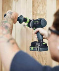 Person using Badass Cordless Drill Driver Featuring Ec Tec Brushless Motor on wooden wall for drilling tasks.