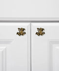 Two gold frog shaped cabinet handles on white cabinet doors, part of the Six Piece Frog Shaped Cabinet Handles Crafted From Solid Zinc Alloy Rust Proof Drawer Pulls And Dope Animal Knobs For Dresser Kitchen Cupboards Quick Mount Screws Included Fly Modern Home Decor Furniture Hardware.