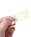 Close-up of hand peeling a circular white adhesive sticker from a yellow backing sheet.