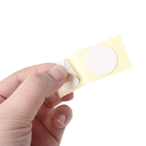 Close-up of hand peeling a circular white adhesive sticker from a yellow backing sheet.